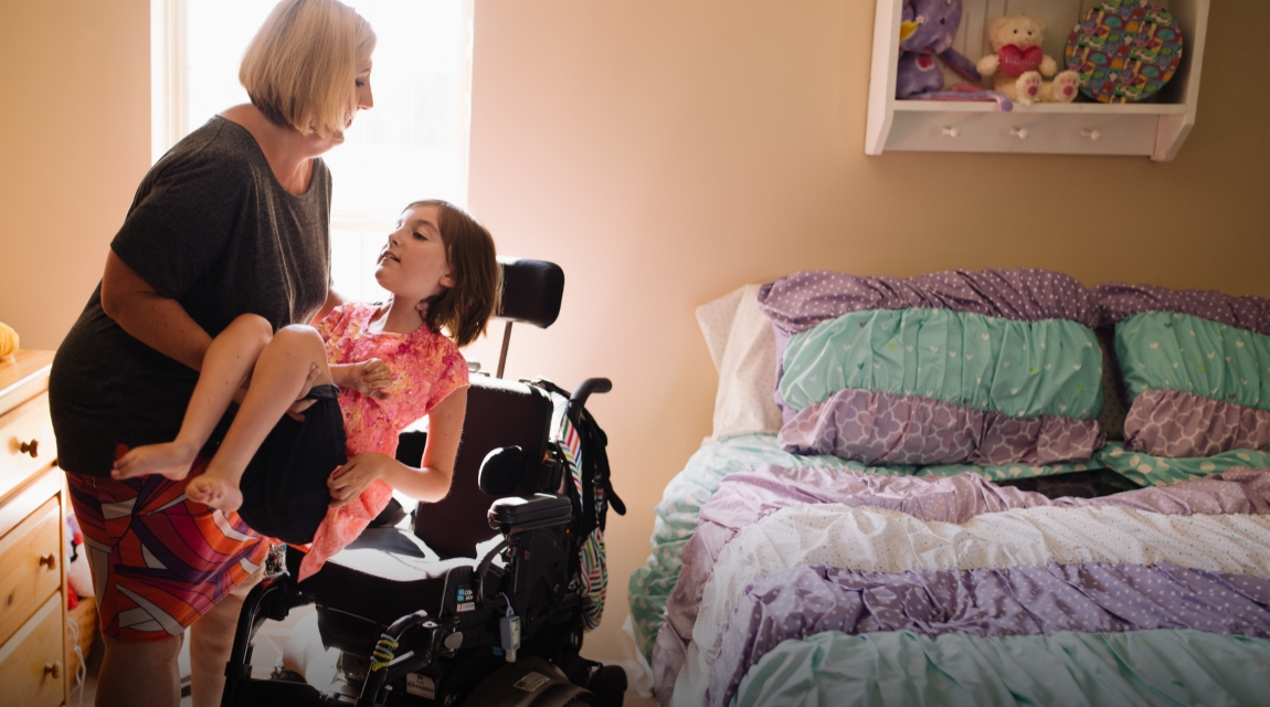 Omaishoitaja auttaa SMA:ta sairastavaa lasta pyörätuoliin